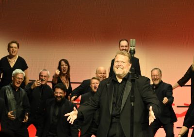 A barbershop chorus - Voices Unlimited from Southern Ontario - performing on stage with lots of animated faces.